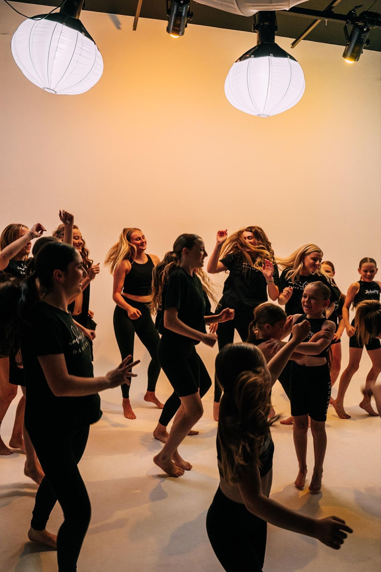 A packed studio of dancers mid-routine under warm light