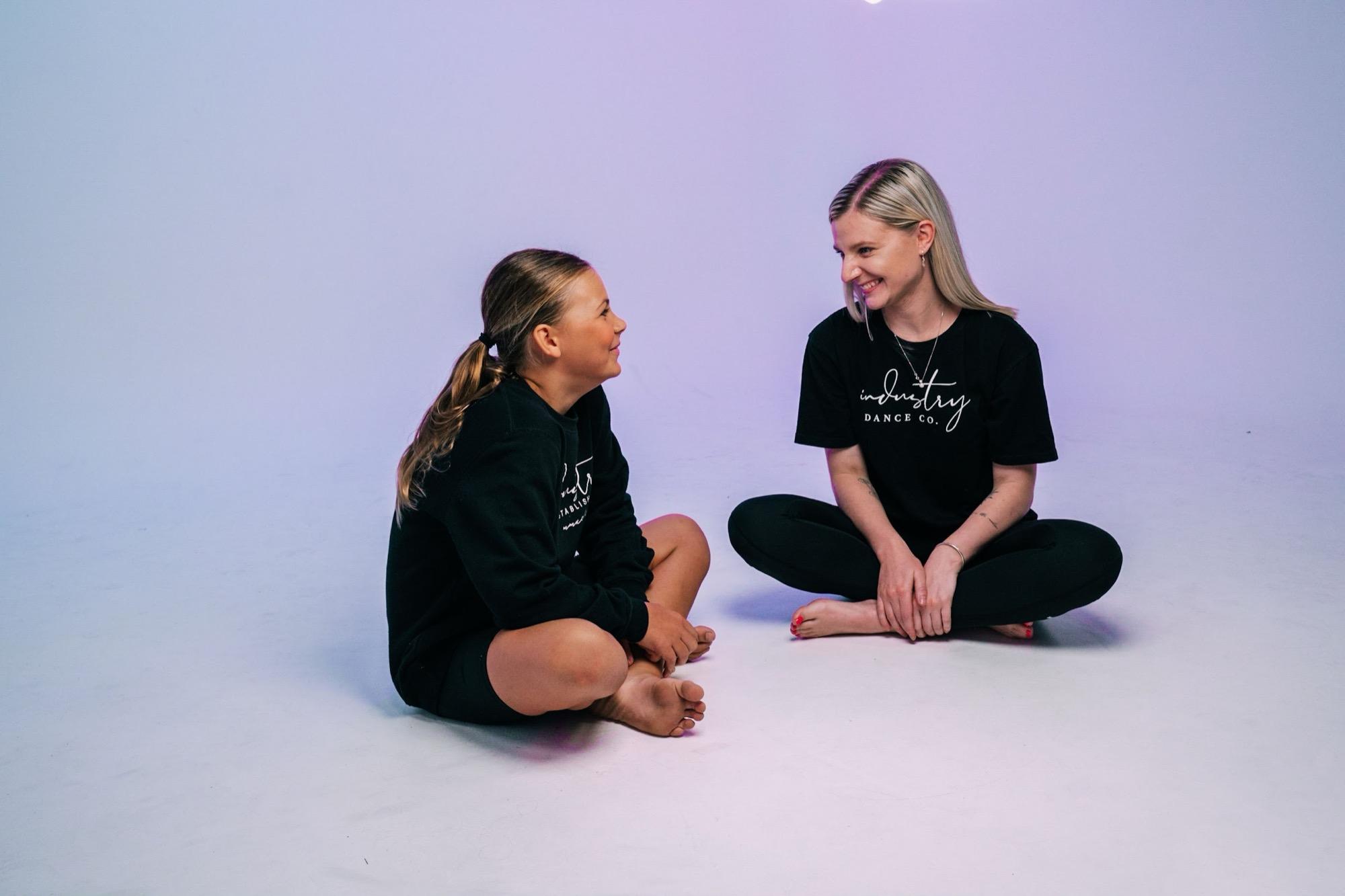 Two IDC teachers deep in conversation on a lilac backdrop