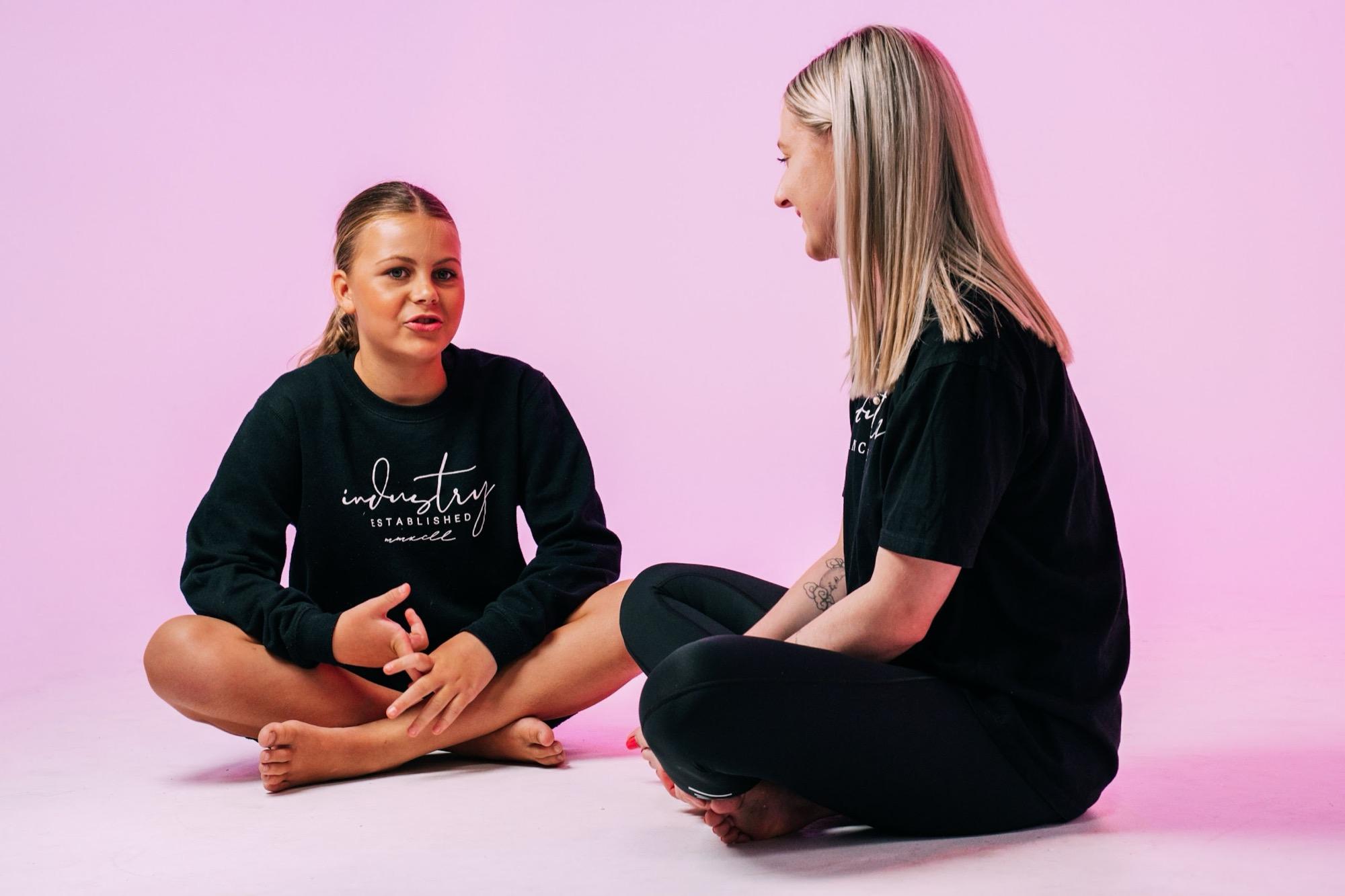 Two IDC teachers sitting cross-legged and chatting on the studio floor