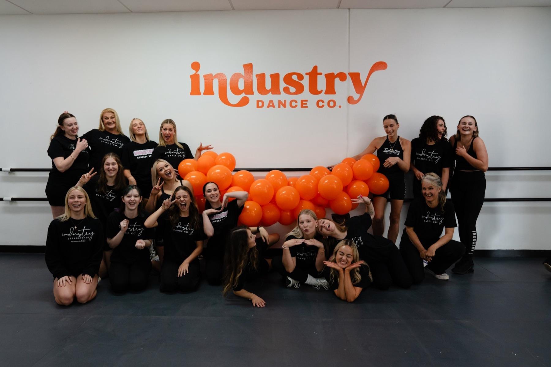 The Industry Dance Co. team being silly in front of orange balloons in the studio