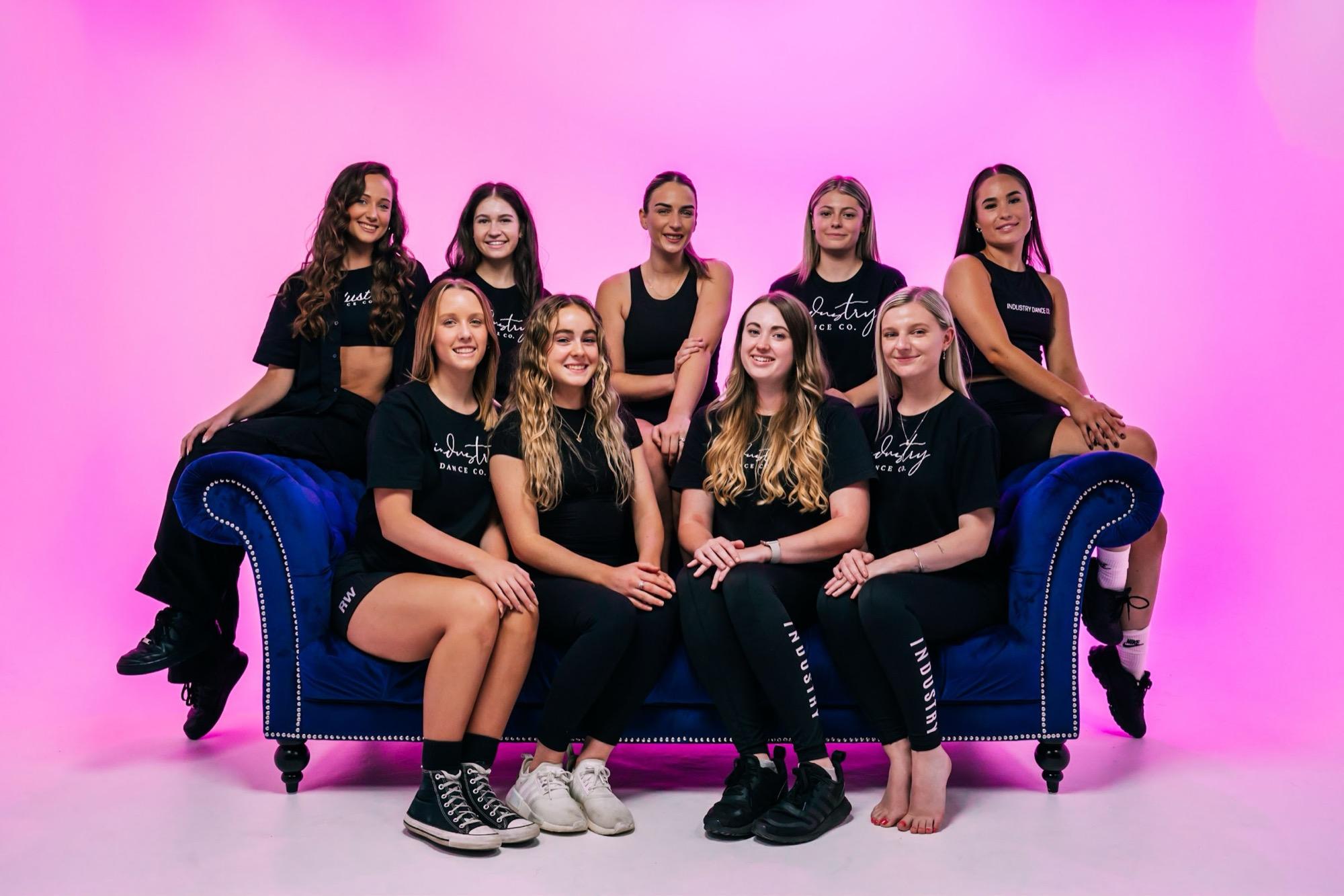 The IDC teachers laughing together on a velvet couch under pink light