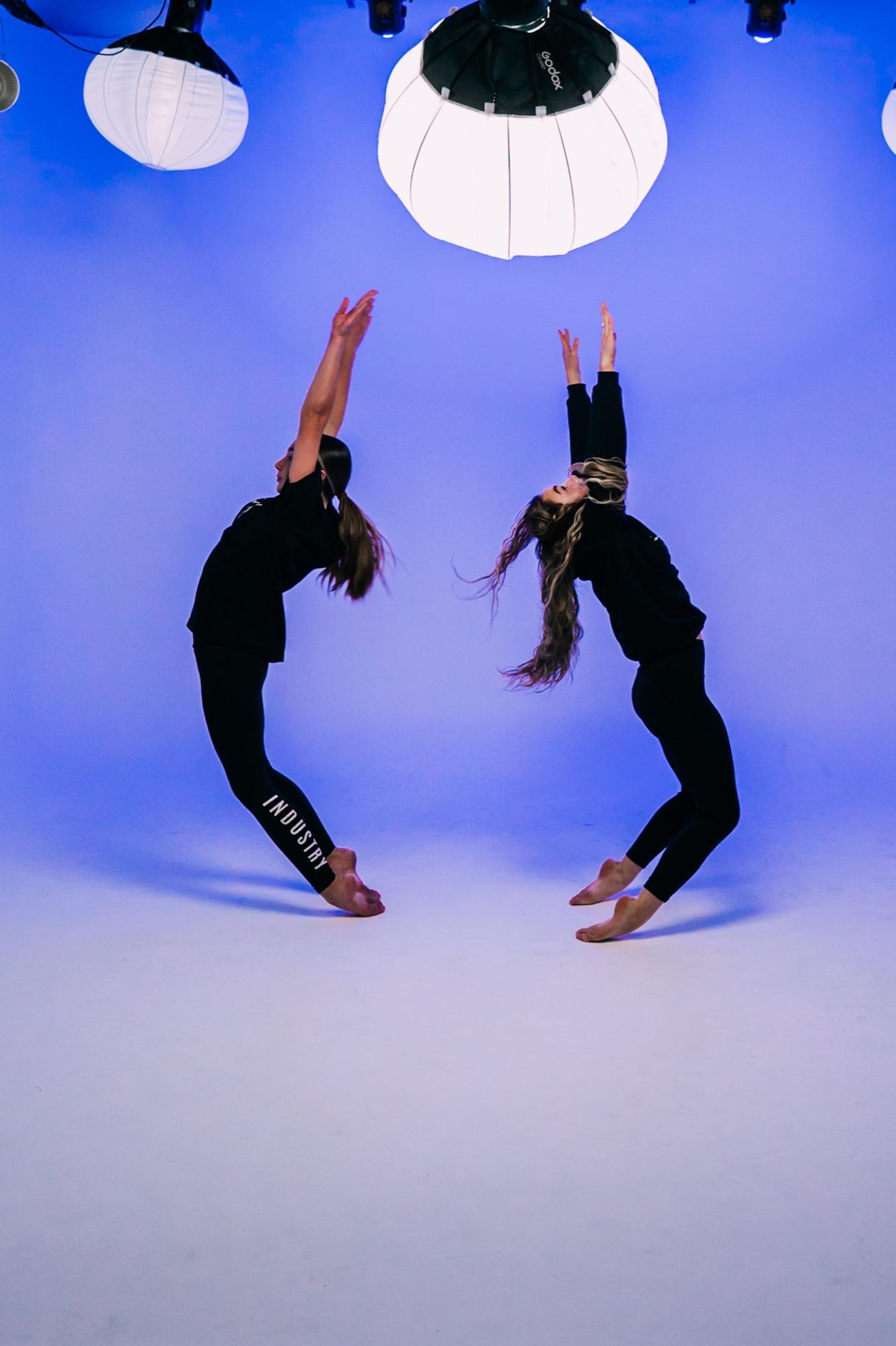 Two dancers in black holding strong backbends against a deep blue backdrop