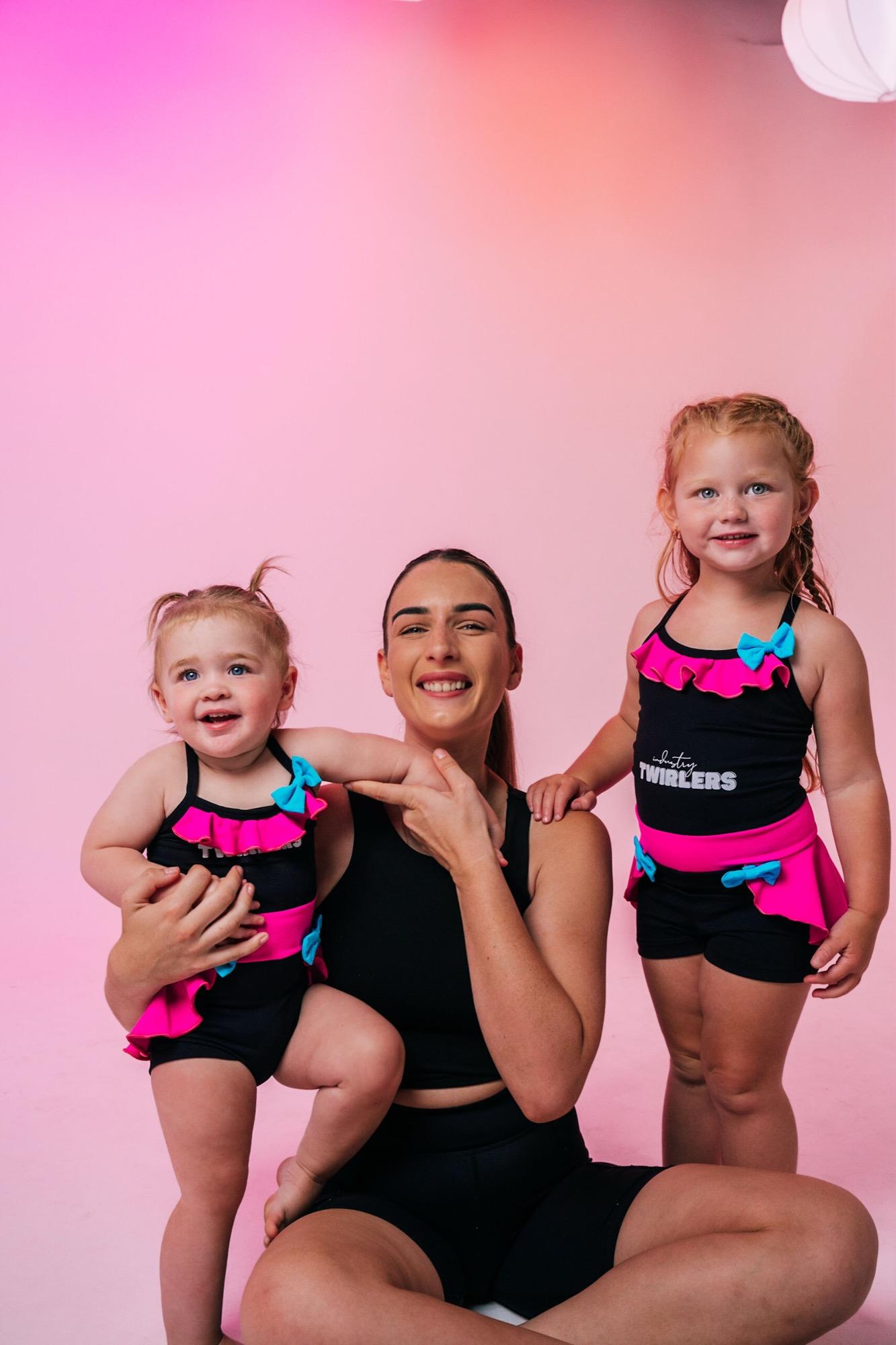 A teacher and two Twirlers sharing a laugh on a pink backdrop